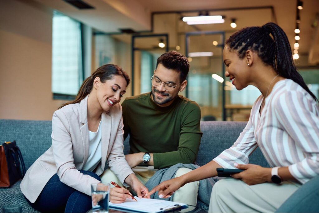 A female loan officer sits with a smiling couple in an office as they sign a contract.