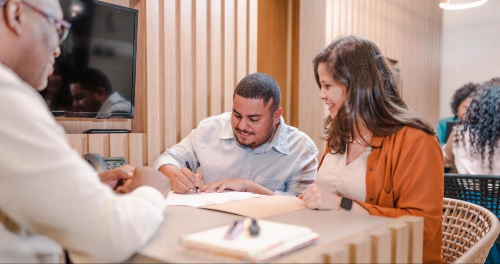 A couple signs mortgage documents in their lender’s office.