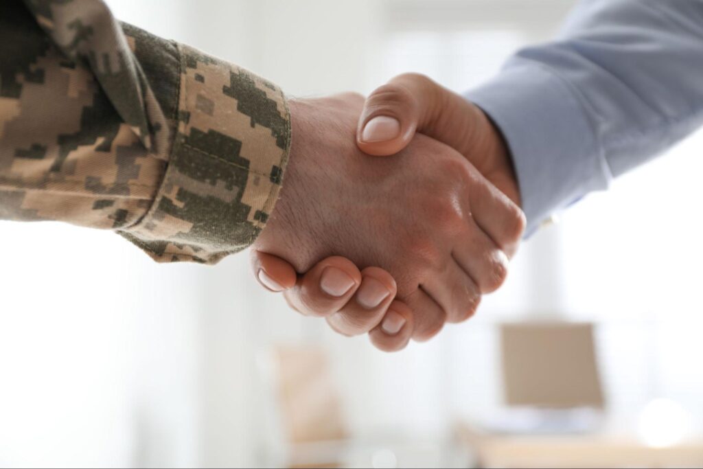 Close up of service member’s hand and a businessman’s hand shaking.