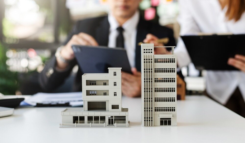 A man and woman speaking while looking at tablets and two real estate mockups in the forefront of the image.