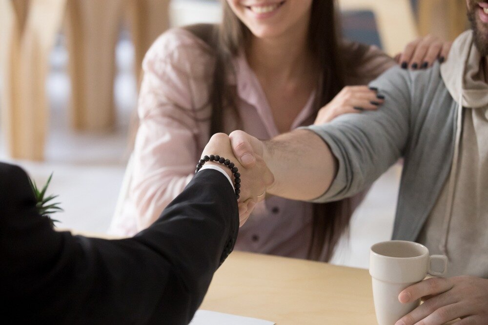 A couple reaches over a table to shake hands with another person.