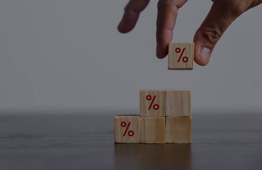 A hand stacking wooden blocks with a red % sign drawn on them.