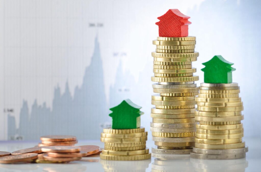 Small green and red model homes sit on top of coins stacked in varying heights.