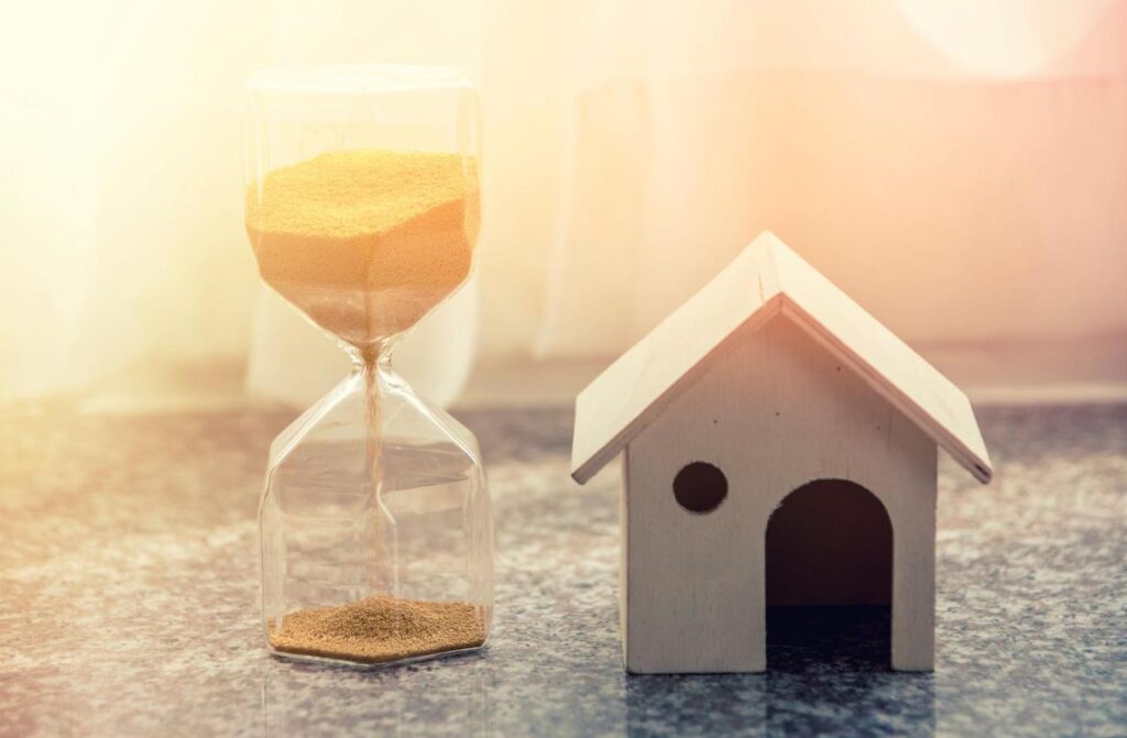 A small model of a house sits next to an hourglass
