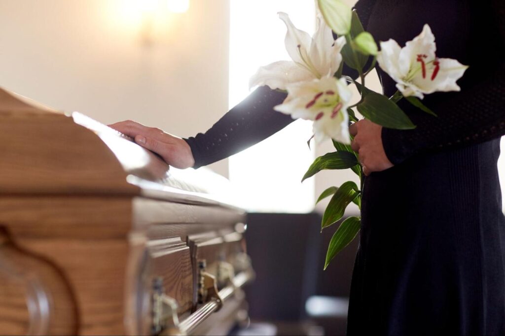 Woman placing hand on casket while holding white lily flowers