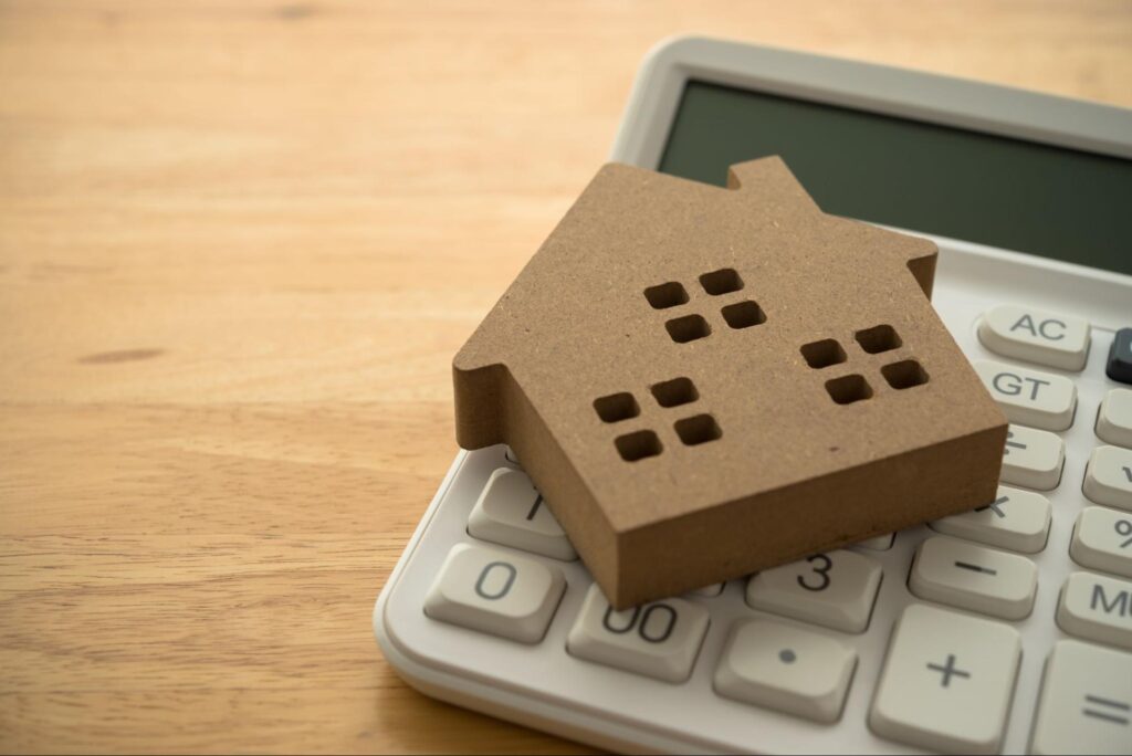 A brown model home sits on top of a handheld calculator.