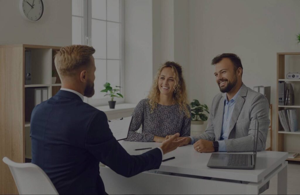A young white couple sitting in a bright office and speaking with their mortgage lender.