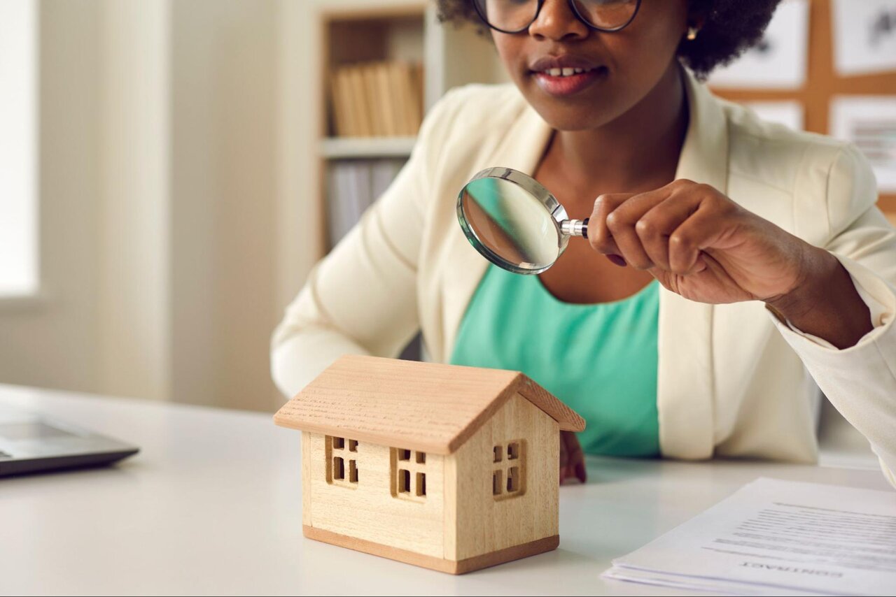 A woman holding up a magnifying glass to a model home.