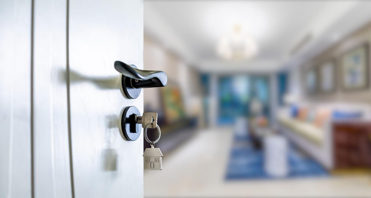 A house key in the lock of an open door leading to a living room.
