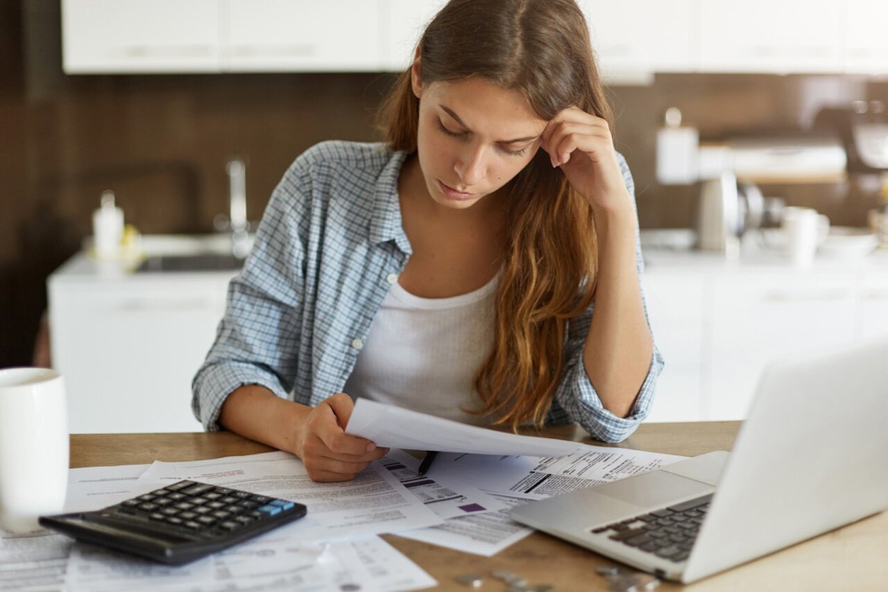 Woman sitting at kitchen table with her laptop and bills in front of her.