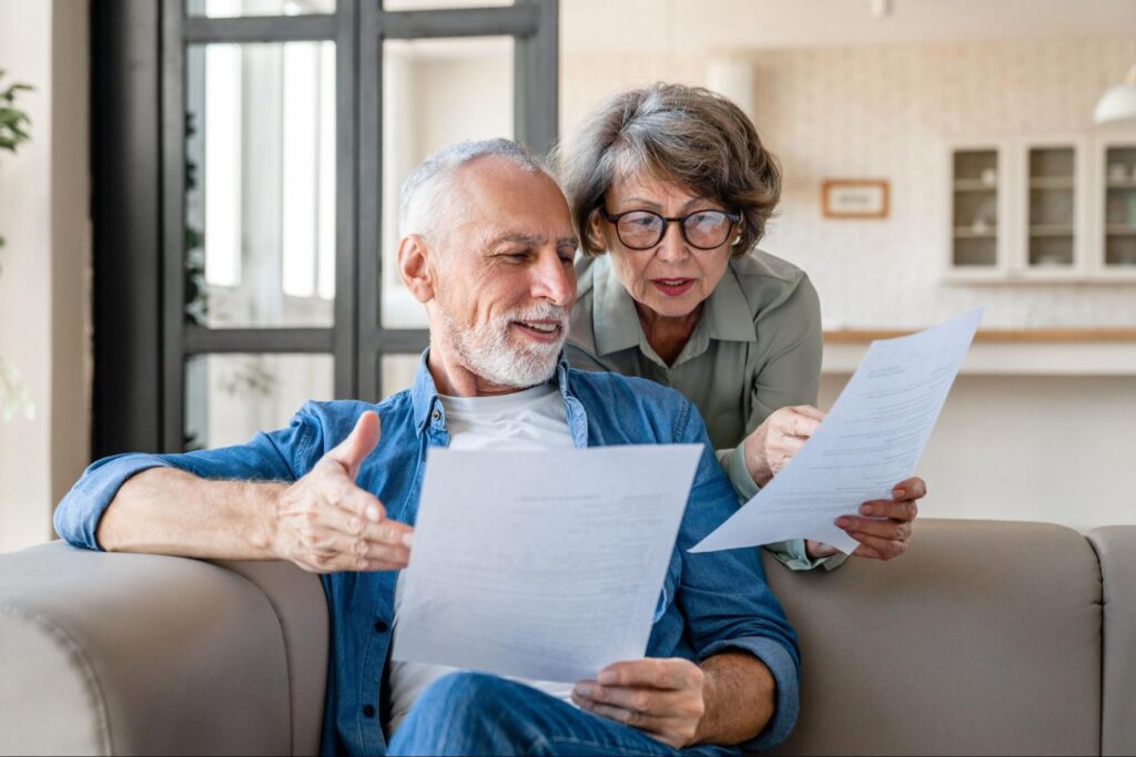 An elderly white couple review documents on their couch.
