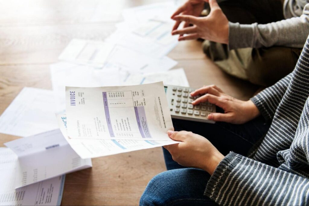 Close up of people calculating bill payments with papers strewn in front of them.