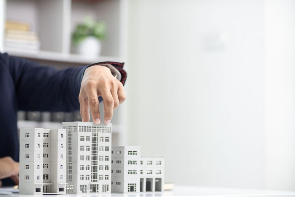 A person in a white office touches the top of a model of a real estate development.