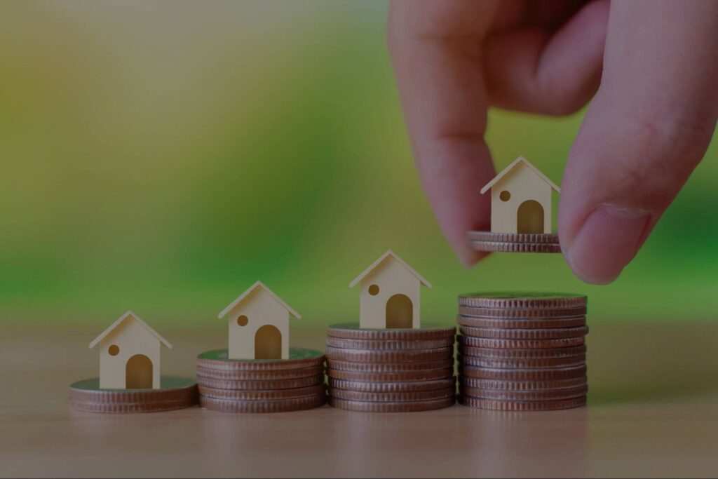 A person places a model home on a stack of coins besides other model homes.