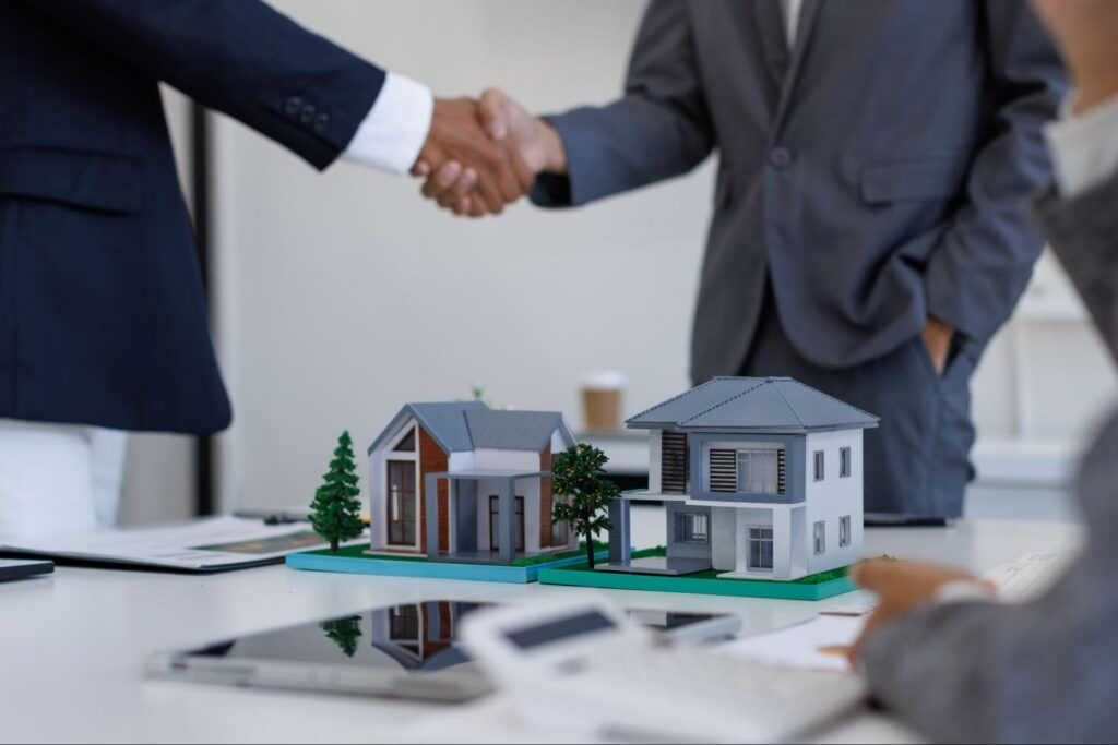 business partners shaking hands behind two model investment properties.