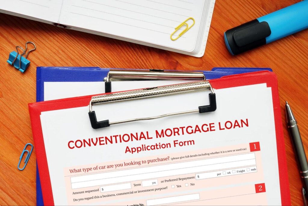 A red clipboard stacked on top of a blue clipboard has a conventional mortgage loan application form attached to it.