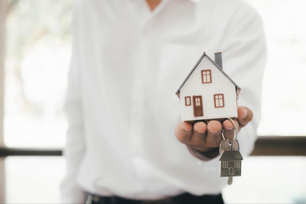 Man presenting a model house and a pair of house keys in his left hand.