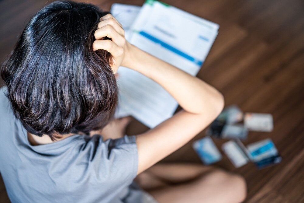 A dark-haired woman holds her head in distress as she reviews her credit card bills.