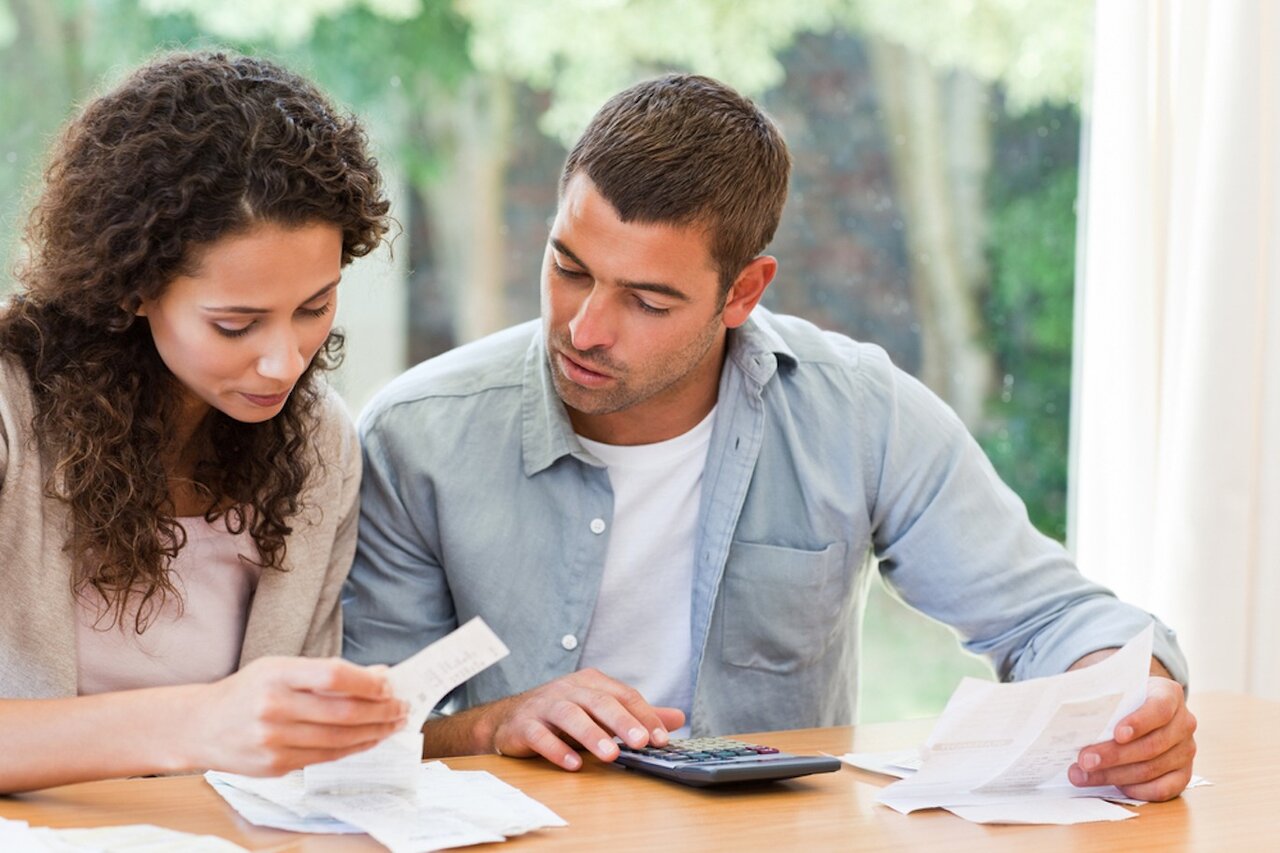 Image of a couple sitting at a table with bills and a calculator in front of them.