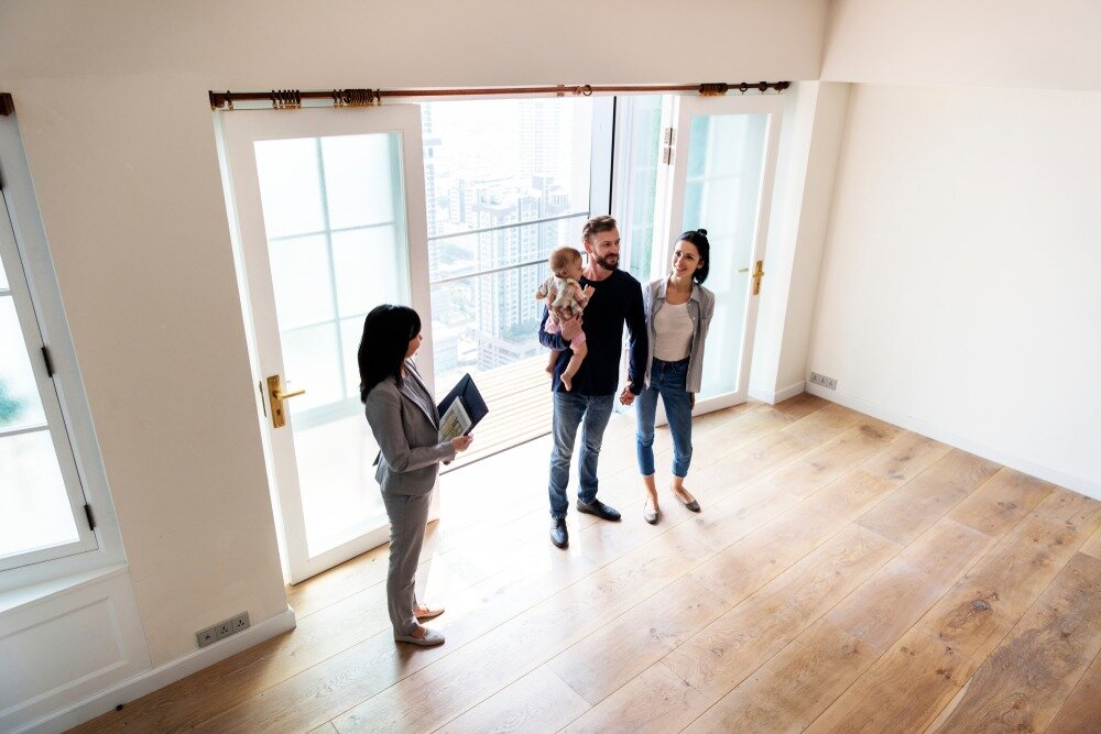 A real estate agent takes a young couple with a baby on a house tour.