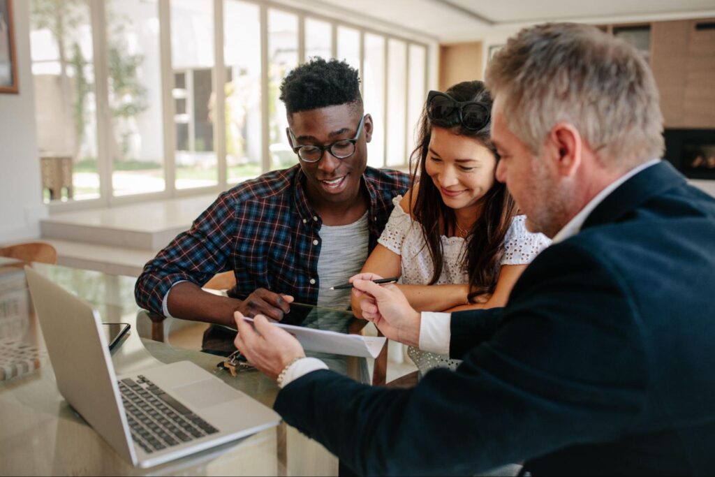 A mortgage lender shows an excited young couple a document.
