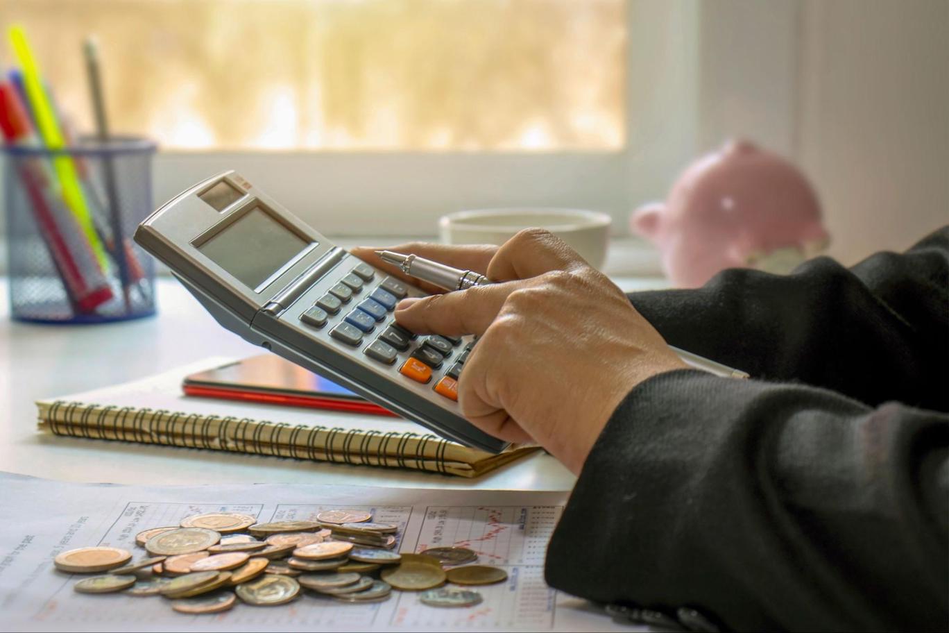 Picture of someone typing on a calculator with money next to them