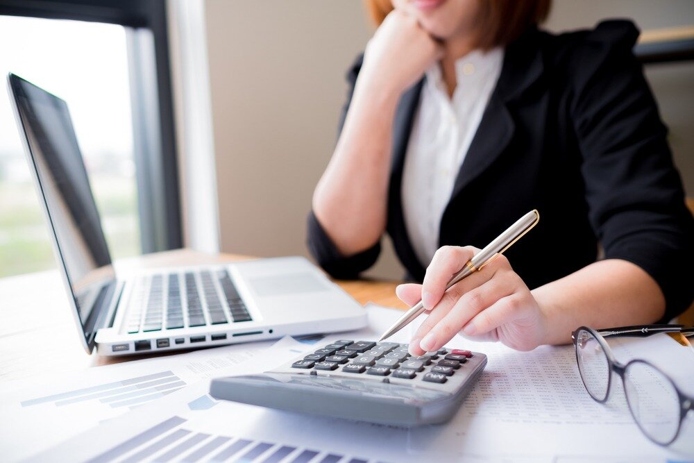 Woman sitting at desk using a calculator and laptop.