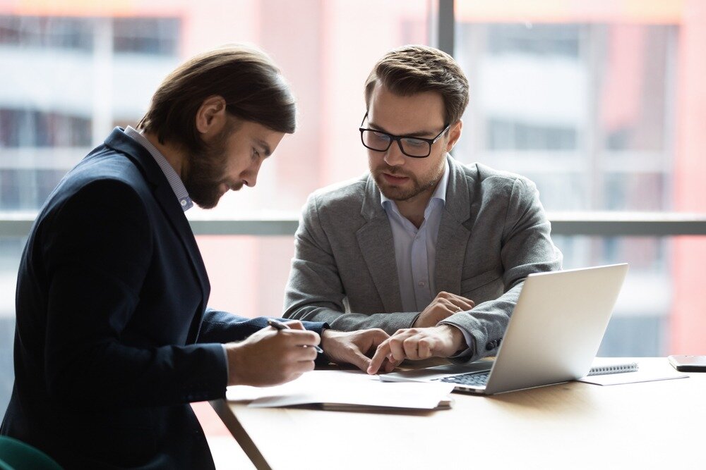 Image of two men reviewing documents at a conference table with a laptop open in front of them.
