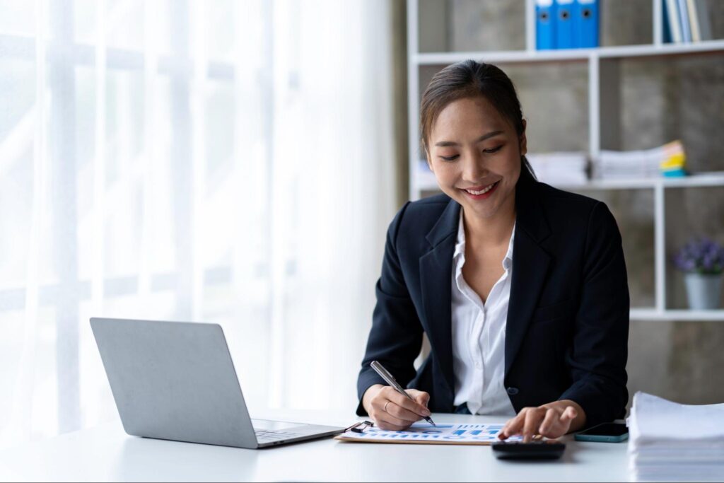 A woman reviews graphs and uses a calculator while sitting in her office.