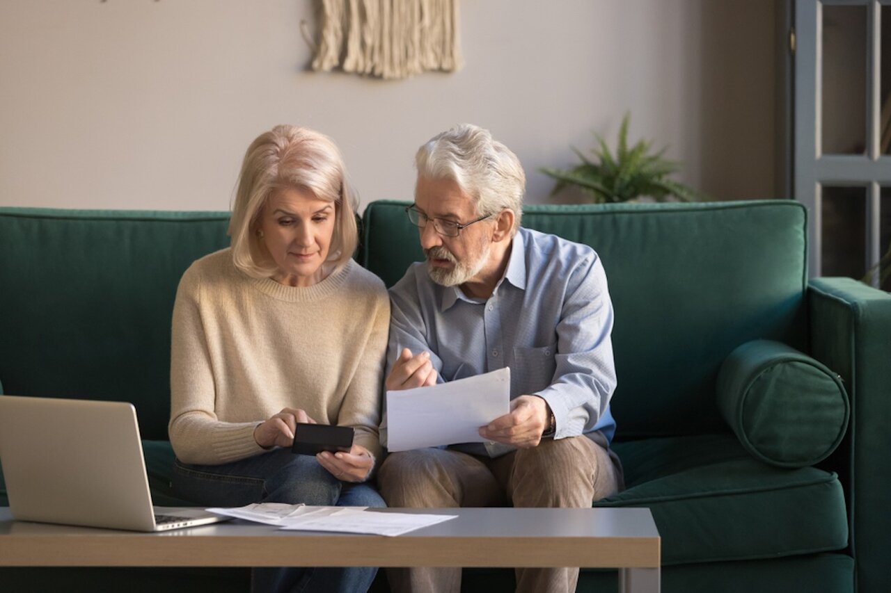 Senior couple sitting on couch calculating their finances.