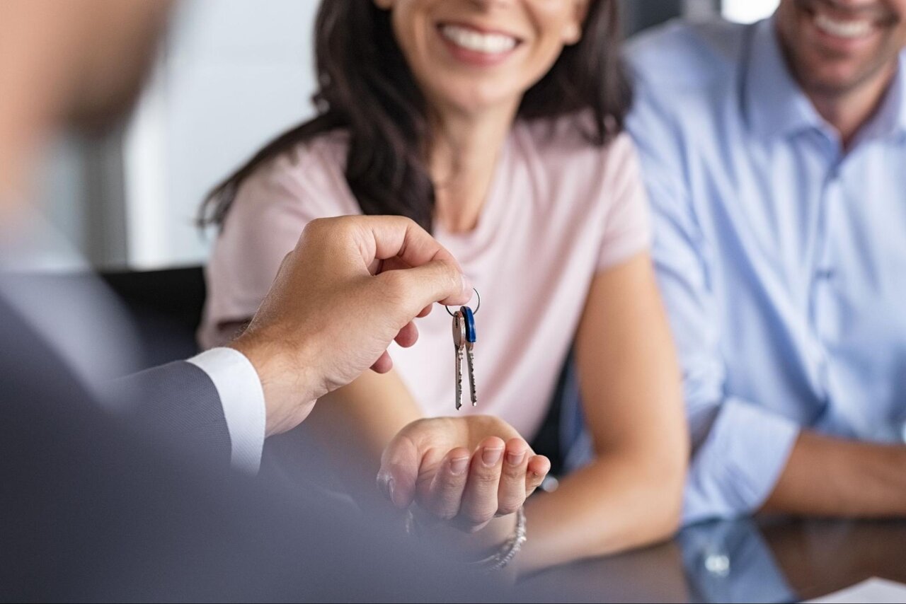 A mortgage lender handing the keys to the home to a smiling couple.