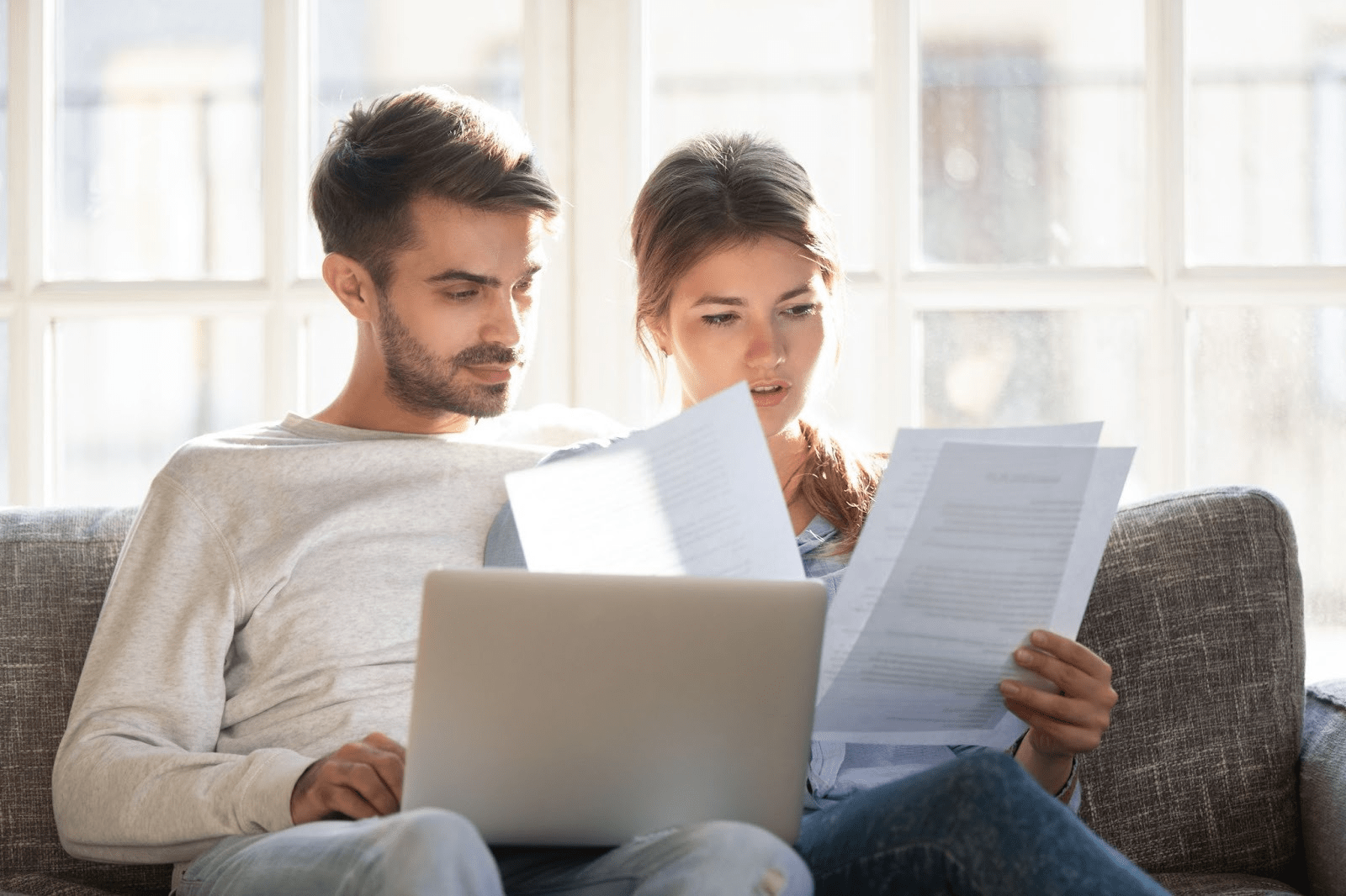 A young couple sorts through documents while sitting on the couch.