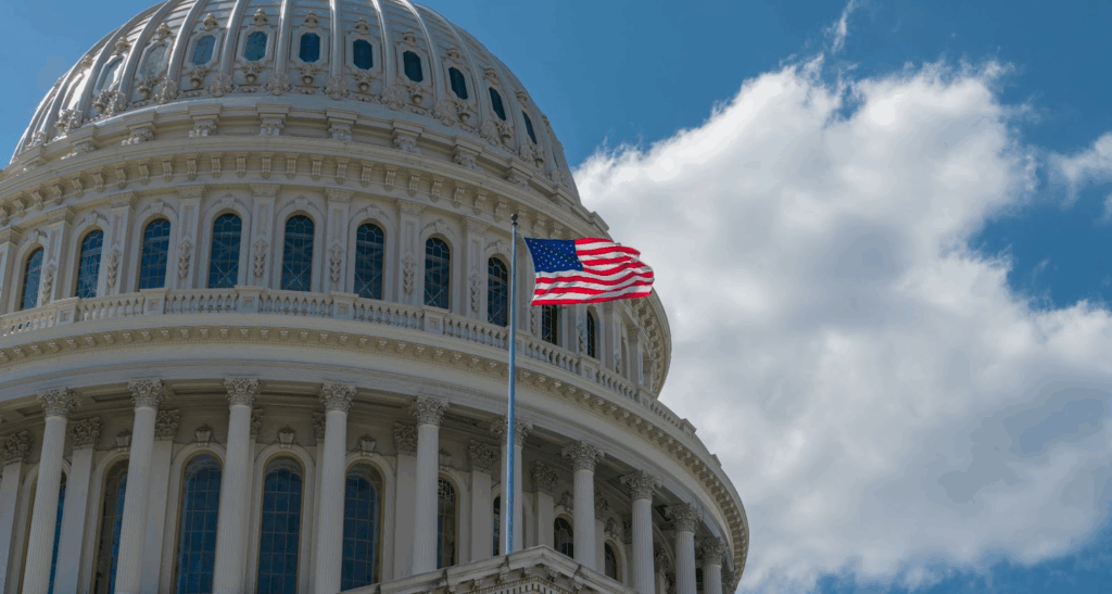 An American flag waving in front of the United States Capitol dome.