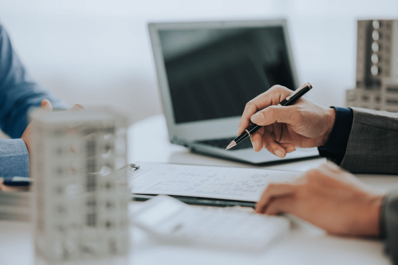 Two people sit at a desk with a laptop and model buildings on it and review a contract.