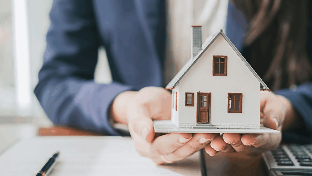 A person holding a small white model home in both of their hands.