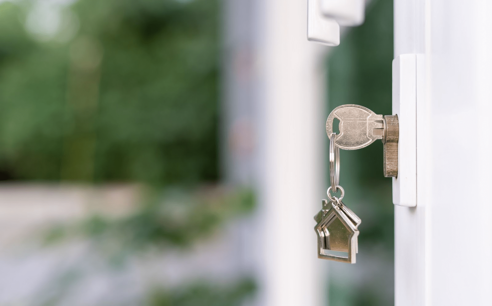 A key in a door with a metal house-shaped keychain attached. 