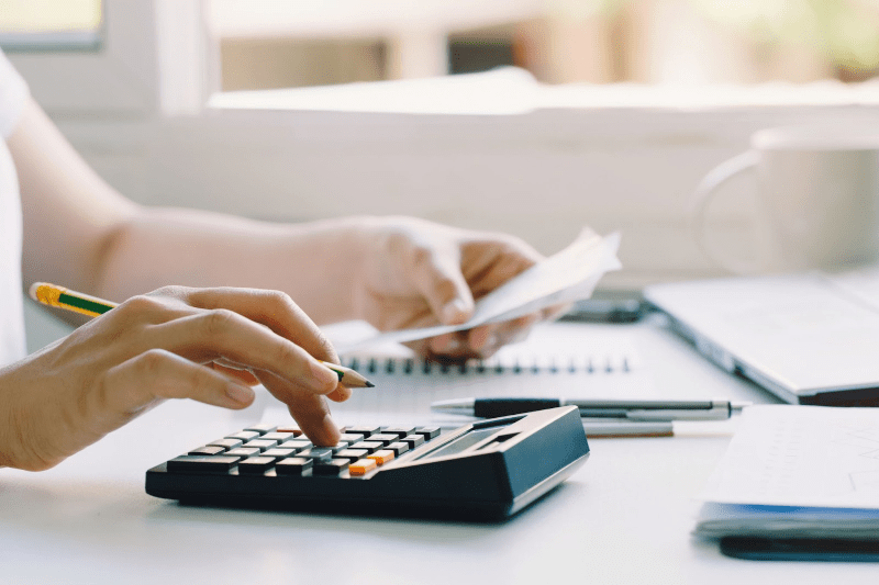 A person typing on their calculator with a pencil in hand.