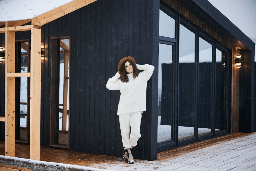 A woman in a white outfit smiling in front of a barndominium in the snow.