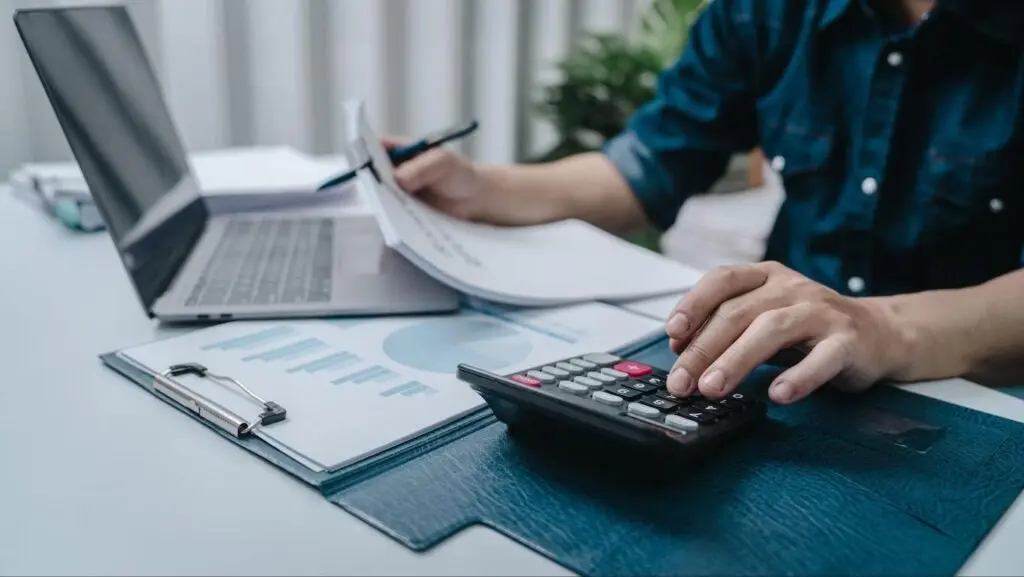 Man sitting at desk with a calculator and paperwork in front of him.