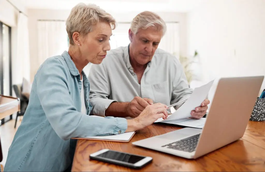 An elderly white couple reviews documents in their living room.