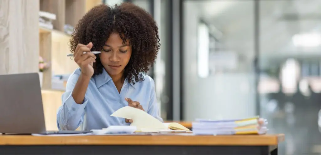 A woman at her desk with a pen in hand going through tax paperwork.