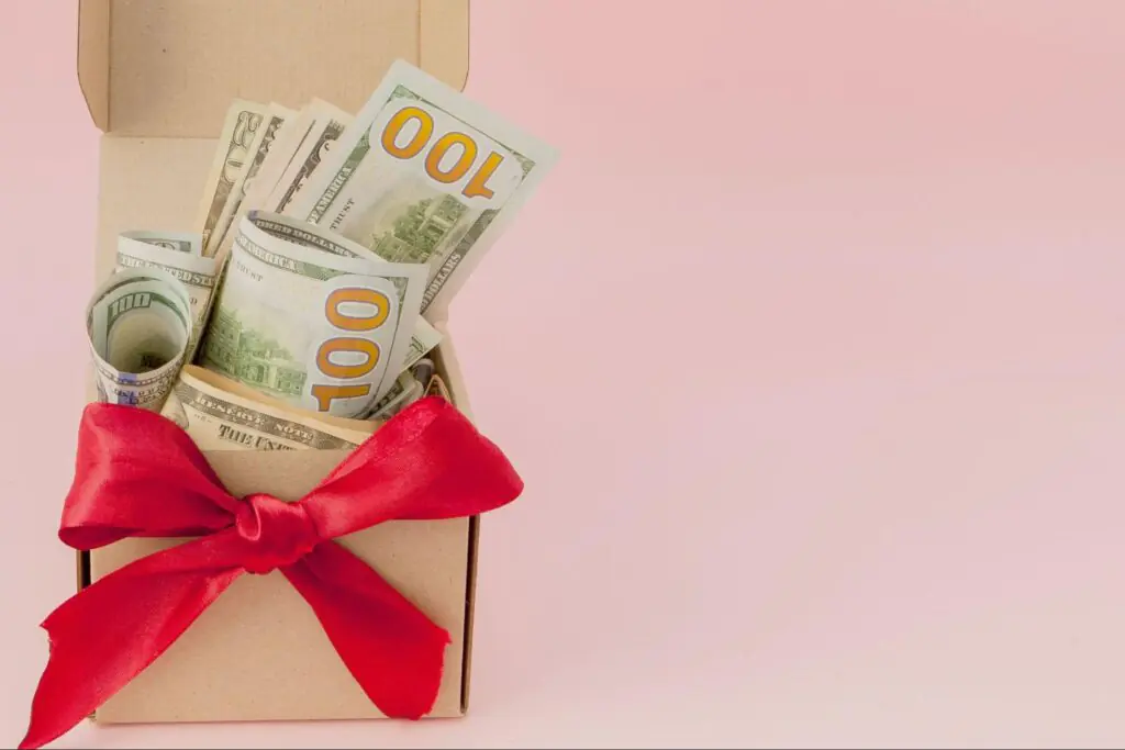 Cash stuffed inside a box with a red bow tied around it.