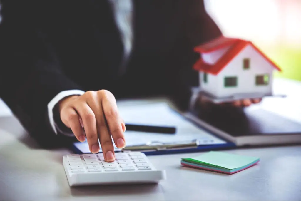 A loan officer holding a red and white model home and typing on a computer.