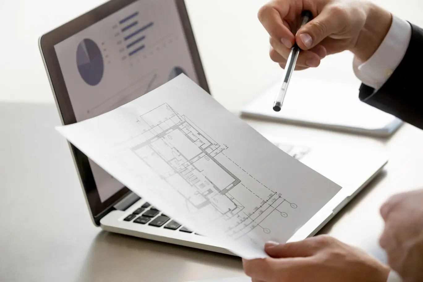 Image of a man looking at a property blueprint with a summary of data on his laptop screen.